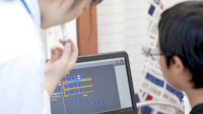 プログラミング画面を見ながら先生に教えてもらう生徒